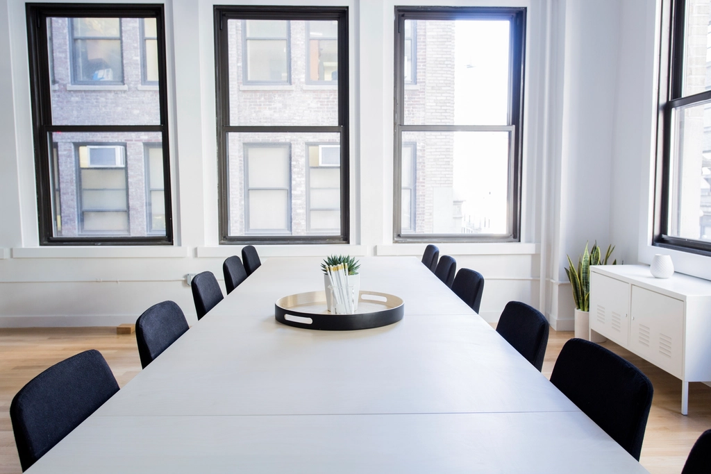 A bright meeting room with a long white table and dark chairs